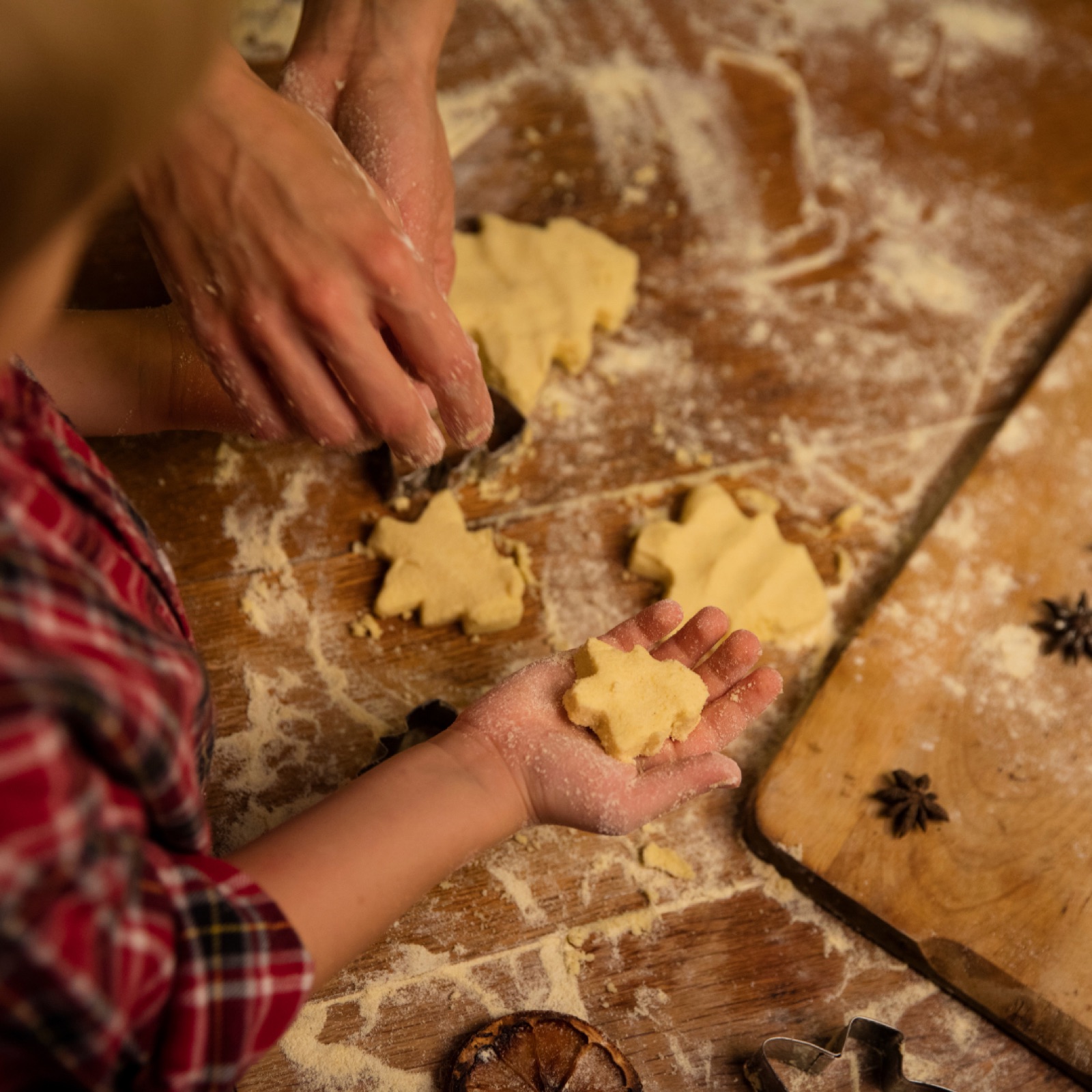Hands make star-shaped cookies on a flour-covered wooden table. Child in plaid shirt, warm and cozy baking scene.