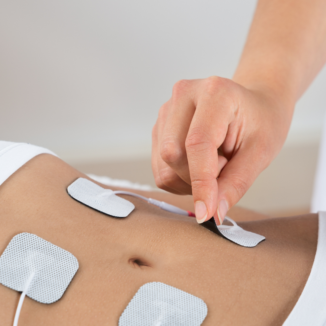Hand applying adhesive pads to a person's abdomen; neutral background, focus on skin and electrodes.