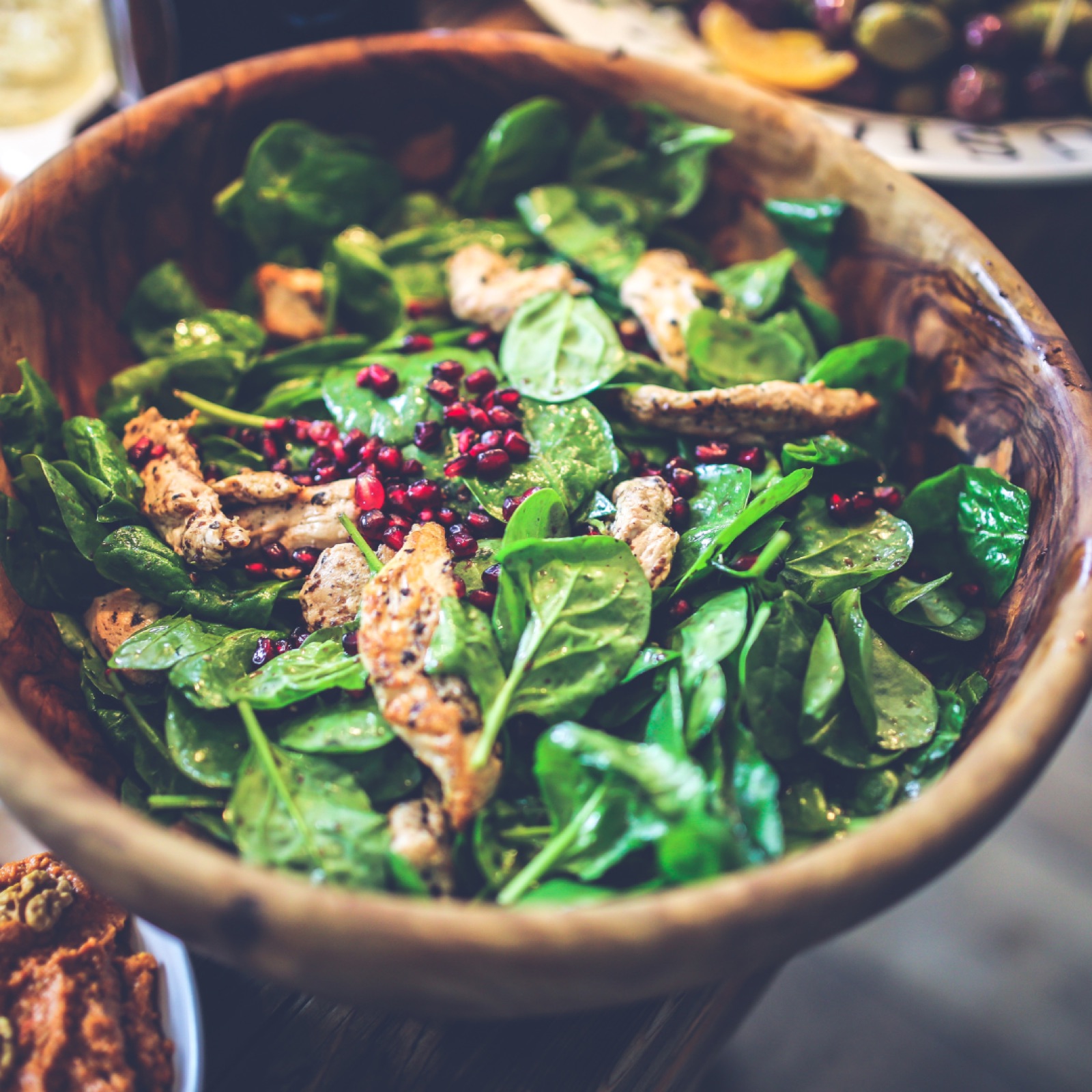 Spinach salad with grilled chicken and pomegranate seeds in a wooden bowl, creating a fresh and vibrant look, perfect for a healthy meal.