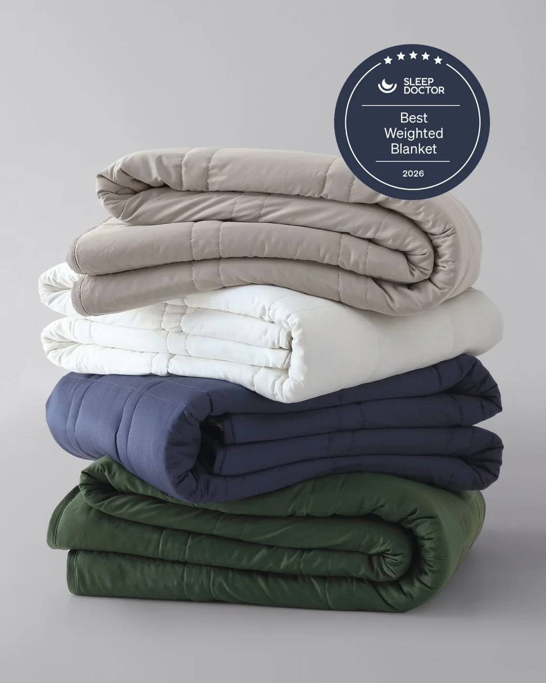 Stack of four folded weighted blankets in beige, white, blue, and green. "Sleep Doctor Best Weighted Blanket 2026" badge on top right.
