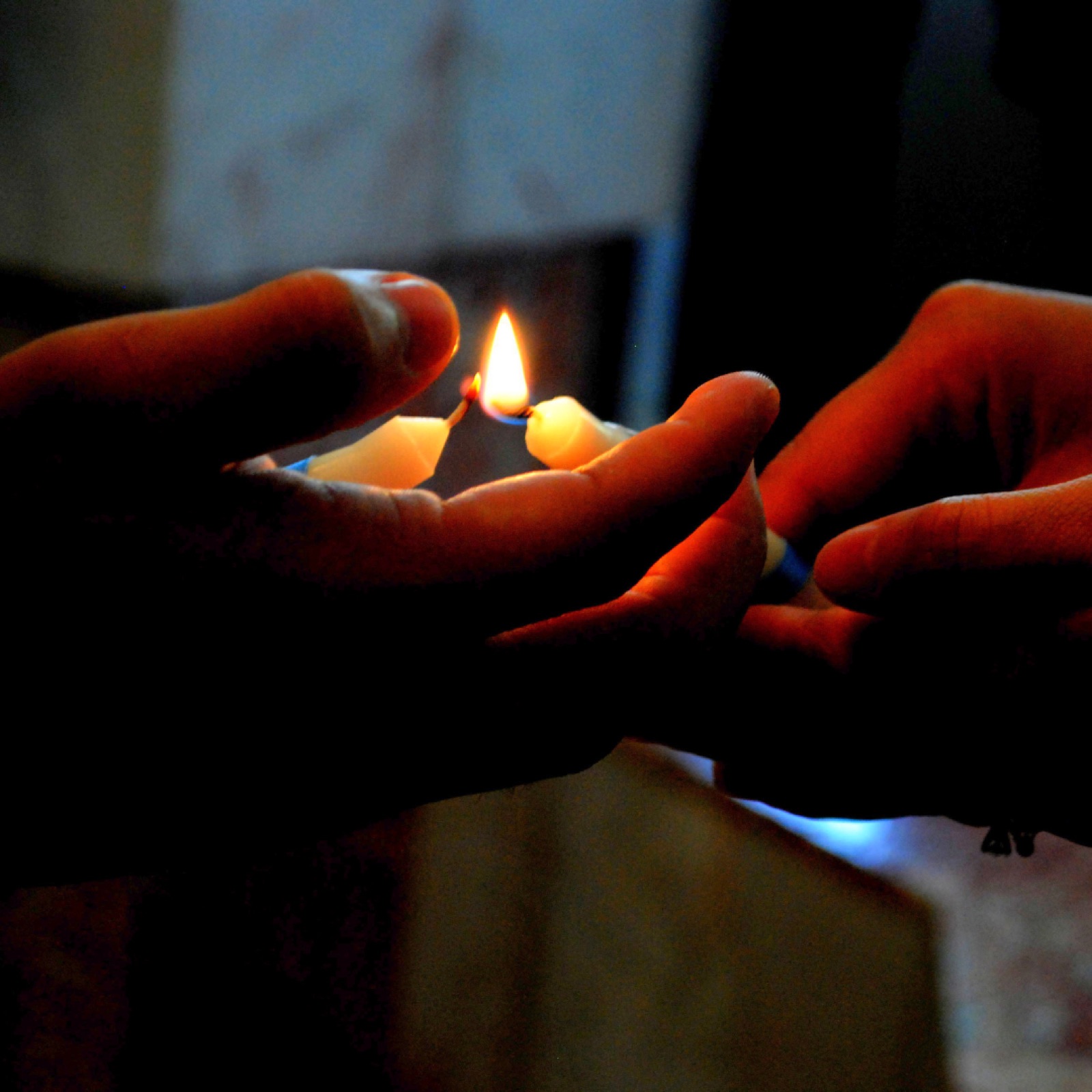 Two hands hold a lit candle with warm glow in a dim setting, conveying a calm, peaceful mood.