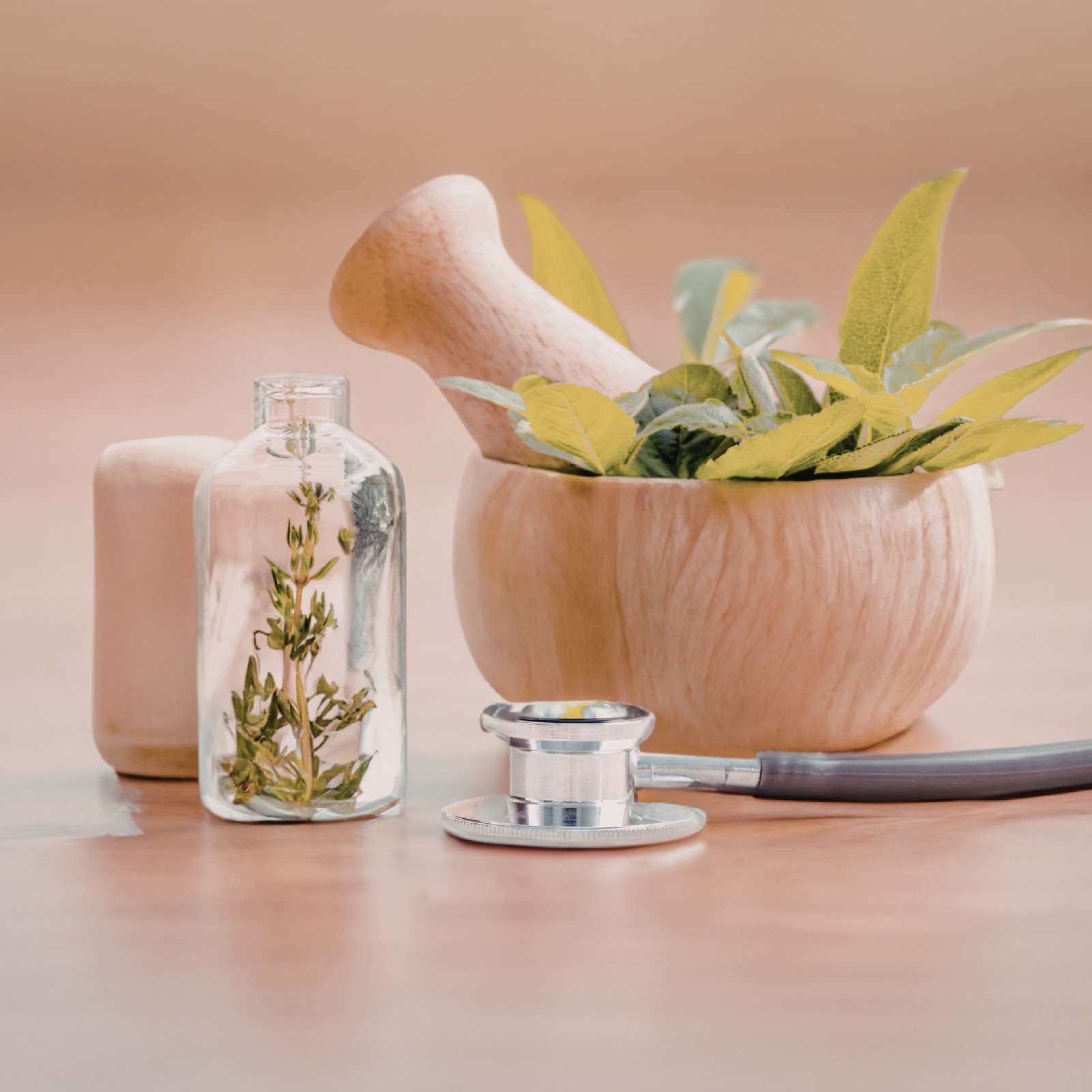 A wooden mortar with herbs, a glass bottle with greenery, and a stethoscope on a light surface, suggesting a blend of nature and medicine.